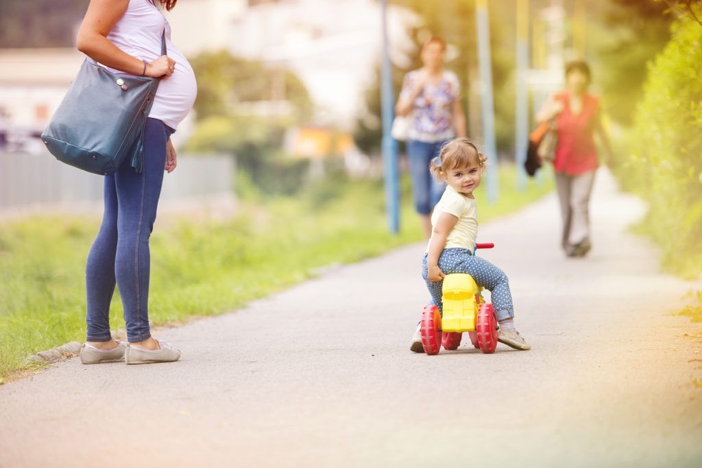 liten flicka åker leksaks bil bredvid en gravid kvinna