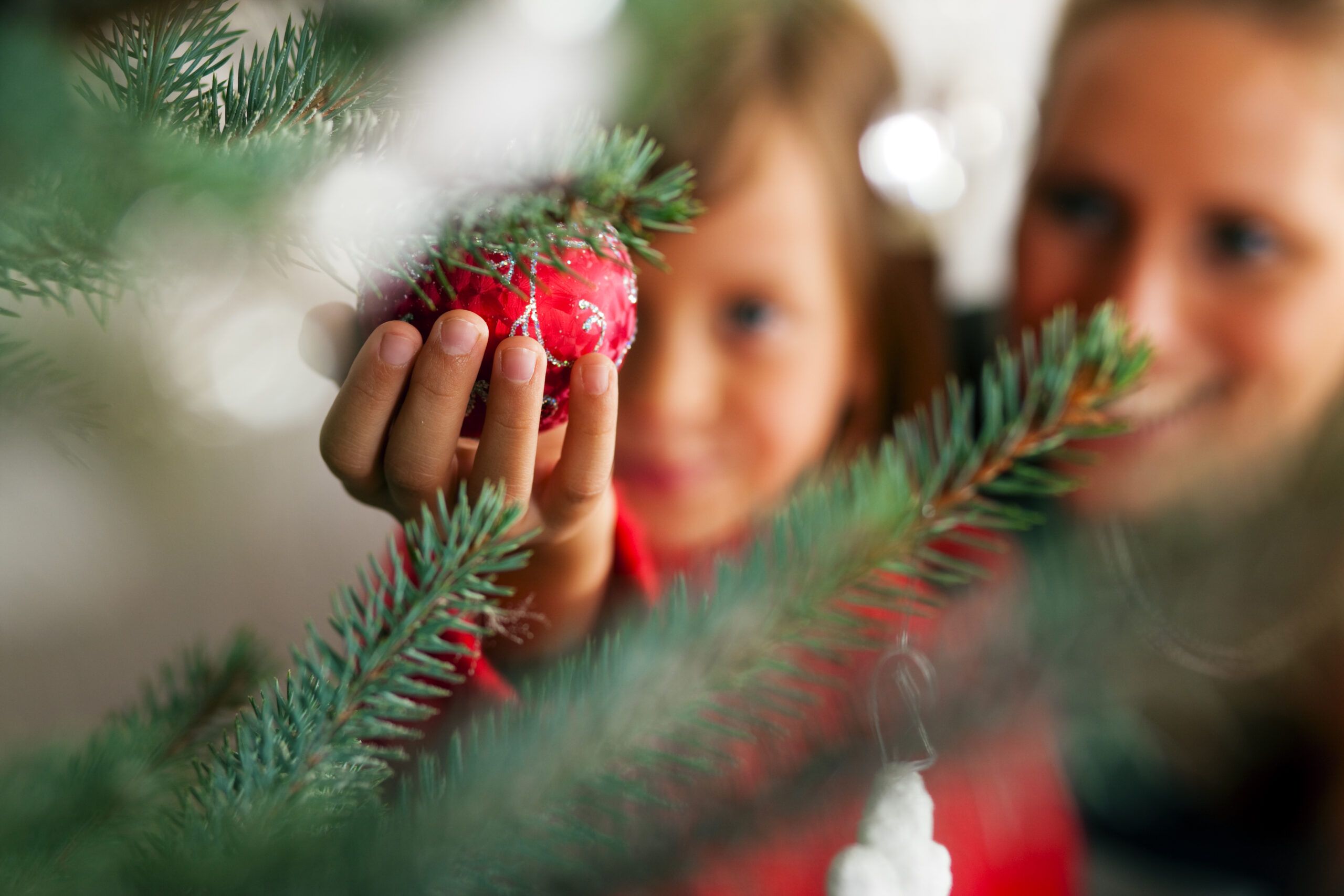 två barn hänger upp en kula i julgranen
