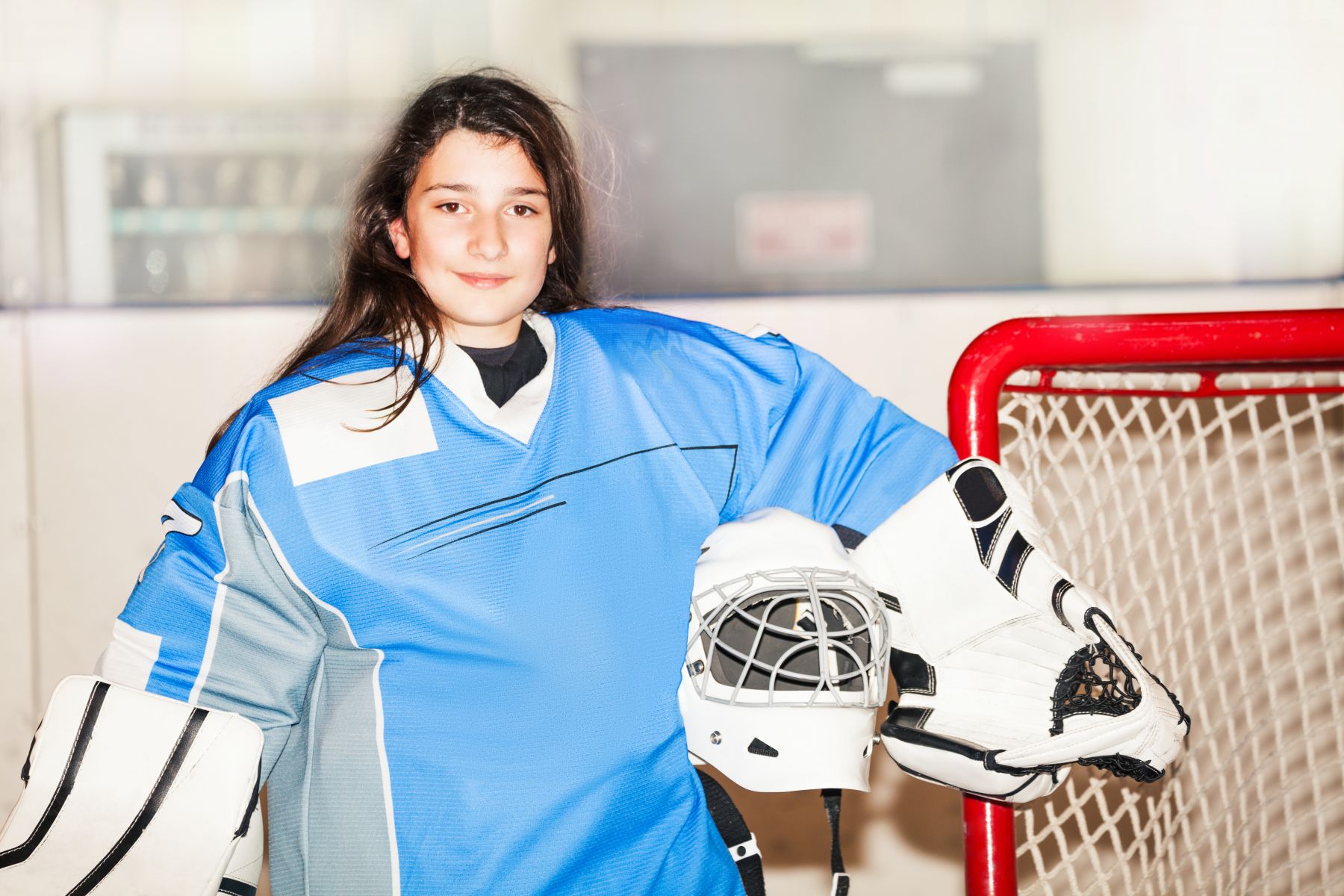 Flicka med hockeyutrustning framför ett ishockeymål
