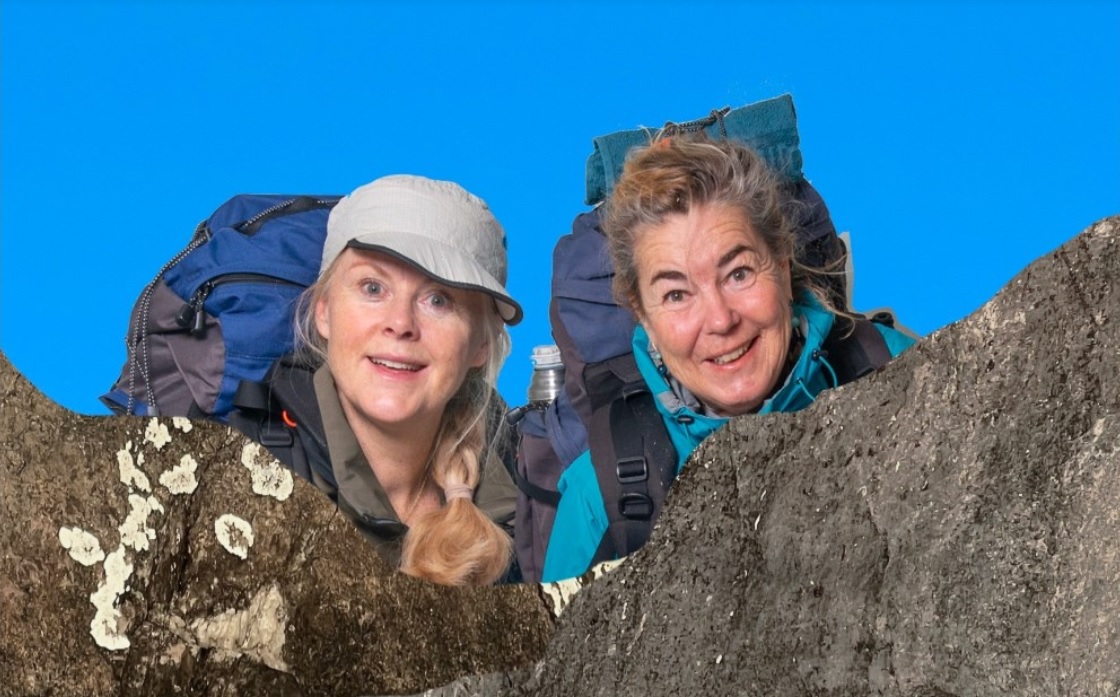 pressbild föreställande två glada kvinnor bakom en stor sten